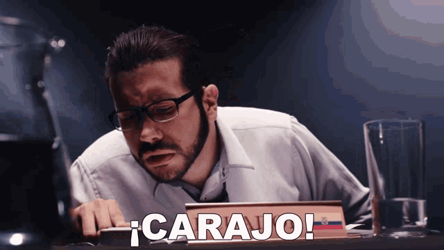 a man with glasses sits at a table with a book that says carajo on it