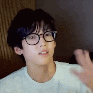 a young man wearing glasses and a white t-shirt is waving his hand .