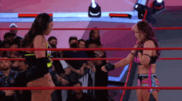 two female wrestlers are shaking hands in a ring .