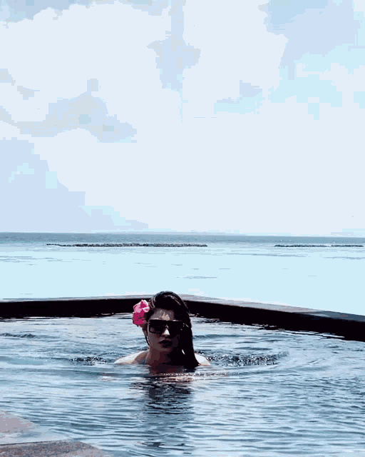a woman wearing sunglasses and a flower in her hair is swimming in a pool