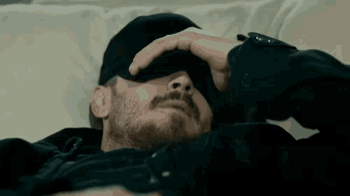 a man with a beard and mustache is laying down with his hand on his forehead