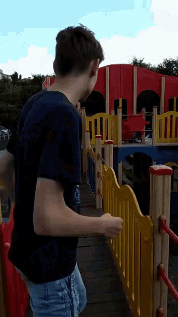 a boy in a black shirt is standing in front of a colorful playground