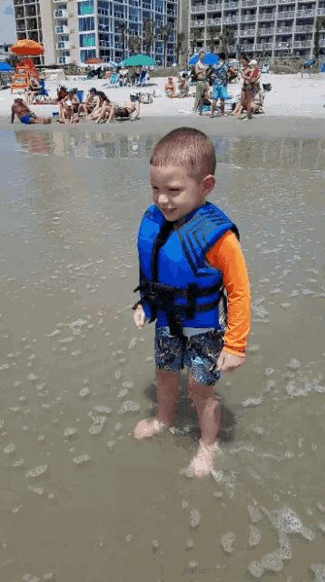 a young boy wearing a life jacket is standing in the water
