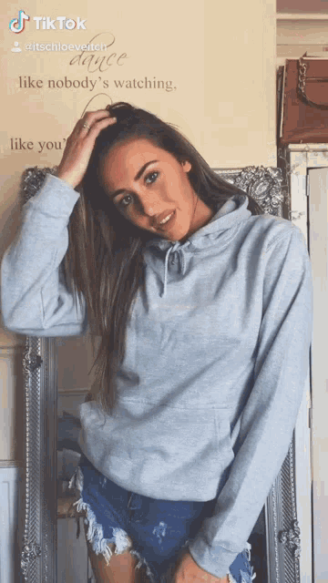 a woman in a grey hoodie is standing in front of a mirror with a quote on the wall that says dance