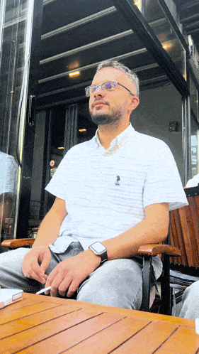 a man wearing a polo shirt sits at a table with a cigarette in his hand