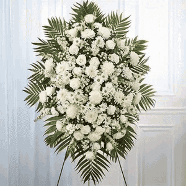 a wreath of white flowers and green leaves is sitting on a stand in front of a door .