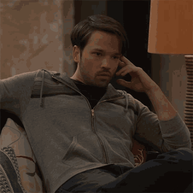 a man in a grey hoodie is sitting on a couch