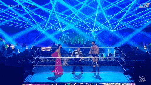a woman in a pink dress is standing in a wrestling ring with a referee .