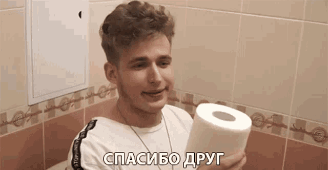 a young man is sitting on a toilet holding a roll of toilet paper in a bathroom .