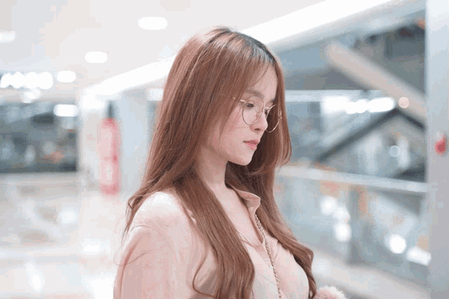 a woman wearing glasses and a pink shirt looks down at something