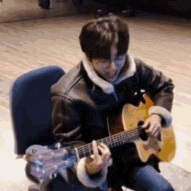 a man in a leather jacket is playing an acoustic guitar .