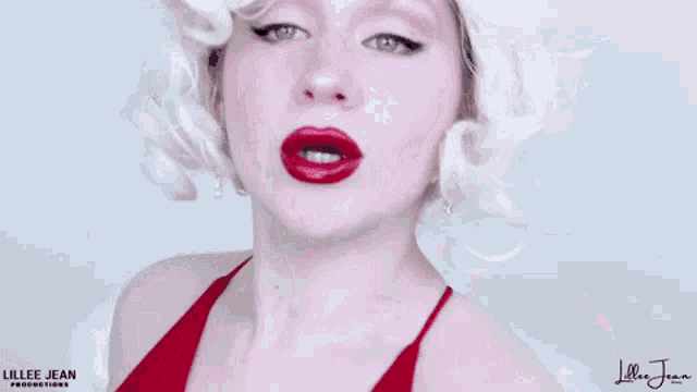 a woman with blonde hair and red lips is wearing a red dress and wig .