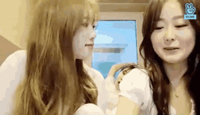 two women are sitting next to each other in front of a window and looking at each other .