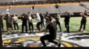 a man is kneeling down on a football field with a group of people standing behind him .