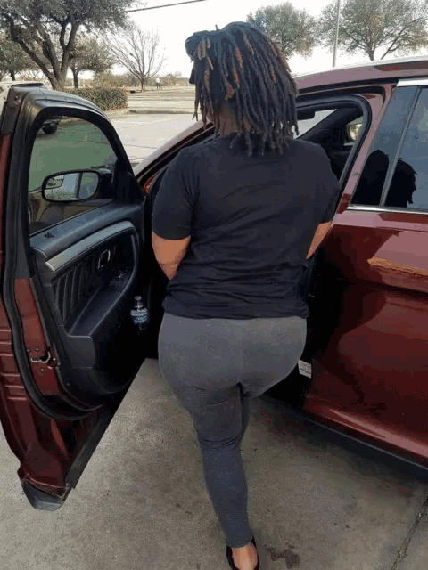 a woman with dreadlocks stands in front of a car