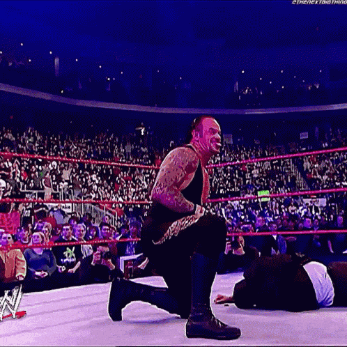 a man is kneeling down in a wrestling ring while another man is laying on the ground .