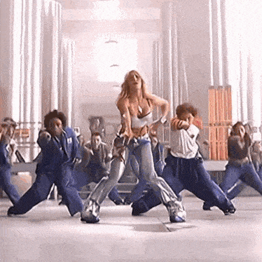 a woman is dancing in front of a group of people in blue uniforms .