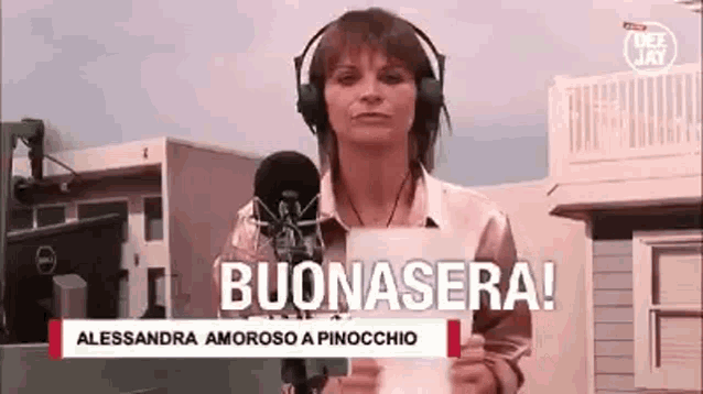 a woman wearing headphones is holding a piece of paper in front of a microphone and says buonasera .