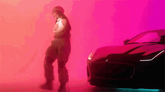 a woman is standing next to a car in a pink room