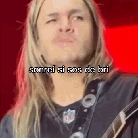a man with long blonde hair is holding a guitar and smiling with the words sonrei si sos de bri above him .