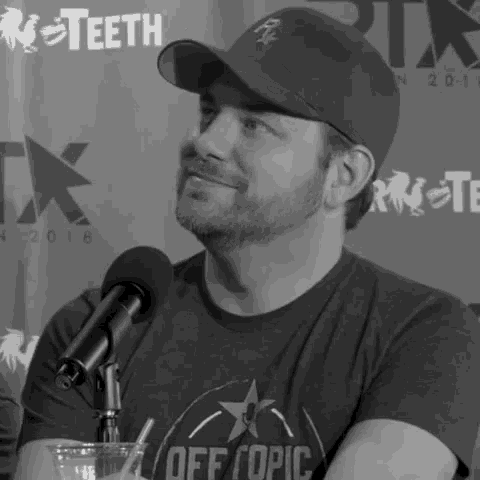 a man wearing a hat and a shirt that says off topic is sitting in front of a microphone