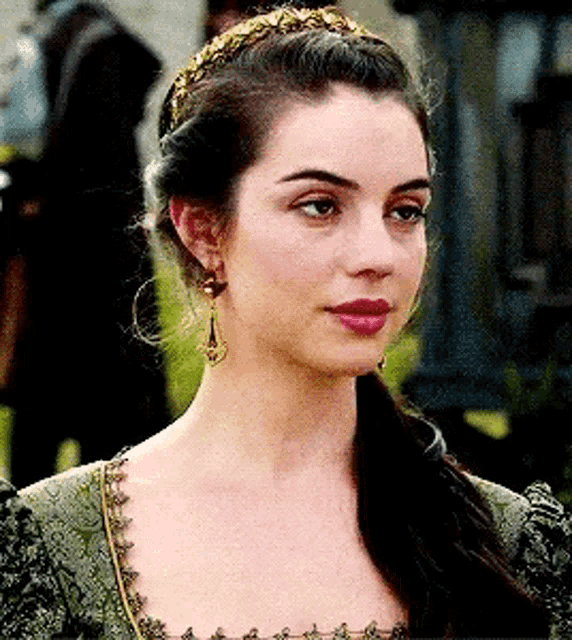 a woman in a green dress and earrings is wearing a headband and earrings .