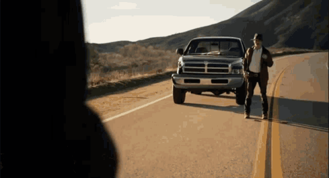 a man is standing next to a dodge truck on the side of a road