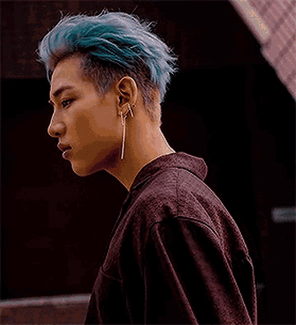 a man with blue hair and earrings is wearing a purple shirt and a burgundy jacket .