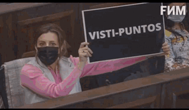 a woman wearing a mask is holding a sign that says visti-puntos .
