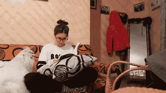 a woman sitting on a couch reading a book while a cat looks on
