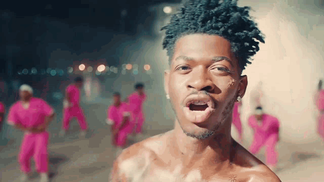 a man without a shirt is standing in front of a crowd of people in pink pants
