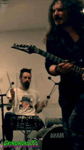 a man playing drums next to a man playing a guitar with grindhorses on the bottom right