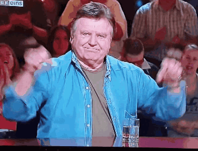 a man in a blue shirt is sitting in front of a crowd with a sign that says reins on it