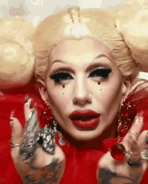 a close up of a drag queen 's face with red lipstick and a lot of rings on her fingers .