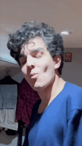 a man with curly hair is wearing a blue shirt and making a funny face
