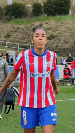 a female soccer player wearing a red and white striped shirt with herbalife on the front