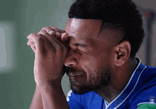 a man in a blue shirt is crying with his hands to his face
