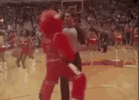 a mascot is standing on a basketball court with a referee .