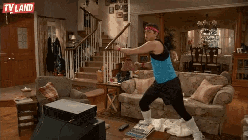a man in a blue tank top is doing exercises in a living room with a tv land logo behind him