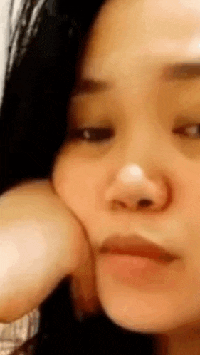 a close up of a woman 's face with her hand on her chin and looking at the camera .