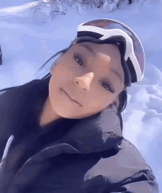 a woman wearing ski goggles and a black jacket is standing in the snow .