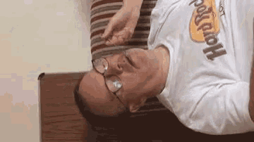a man wearing glasses and a hard rock t-shirt is laying down on a couch .