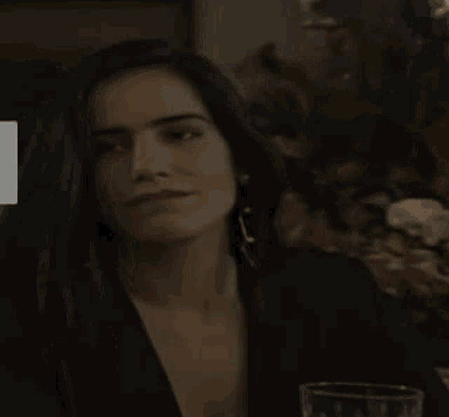 a woman in a black jacket and earrings is sitting at a table with a glass of wine .