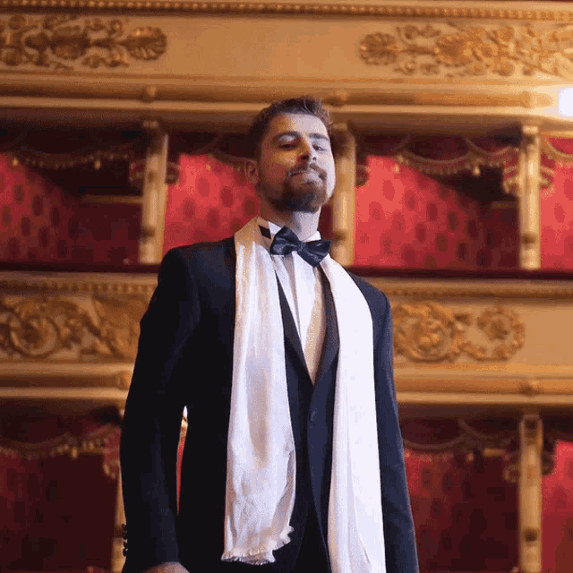 a man in a tuxedo with a white scarf around his neck and bow tie