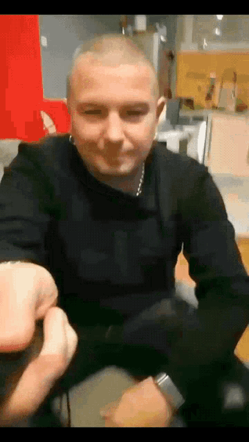 a man with a shaved head wearing a black shirt and a silver watch