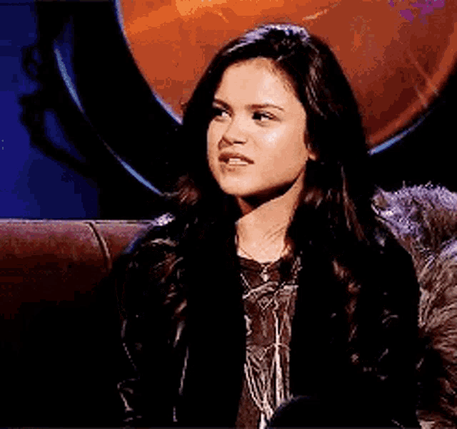 a woman is sitting on a couch making a funny face while wearing a black jacket .