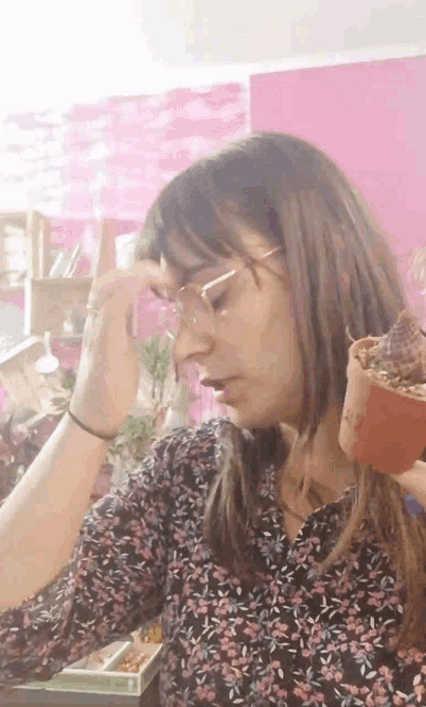 a woman with glasses holds a potted plant in her hand
