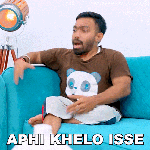 a man in a panda shirt sits on a blue couch with the words aphi khelo isse below him