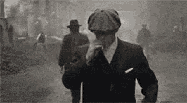 a man in a suit and hat is smoking a cigarette while walking down a street .