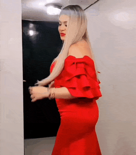a woman in a red dress with ruffled sleeves is standing in front of a door .